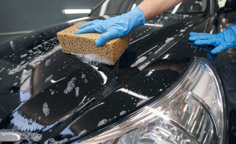 Car detailer washing black vehicle with sponge